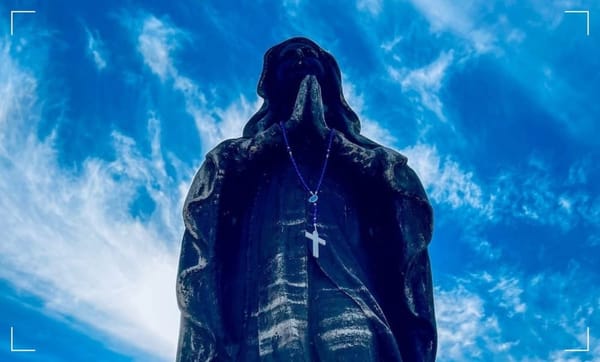 statue of the virgin mary praying with folded hands with a cloudy bluesky background